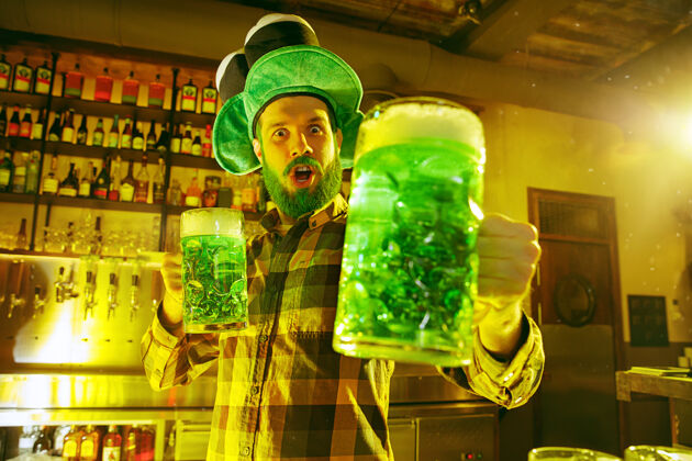 白天快乐的男人拿着一杯啤酒在酒吧里看着一边爱尔兰人玻璃杯马克杯