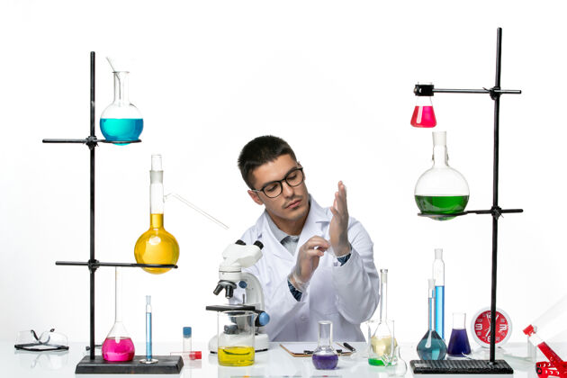 溶液正面图身穿白色医疗服的男性化学家戴着手套坐在白色背景上病毒实验室共患疾病科学手套套装罐子