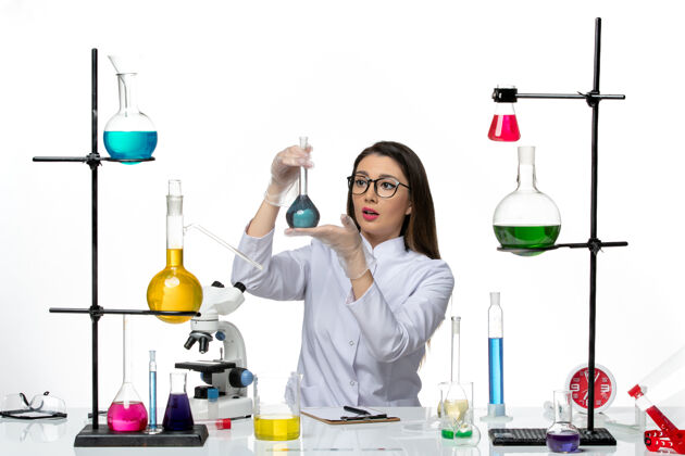 药品前视图：穿着白色医疗服的女化学家拿着装有蓝色溶液的烧瓶 背景是白色的实验室科学病毒冠状病毒大流行容器实验室视图