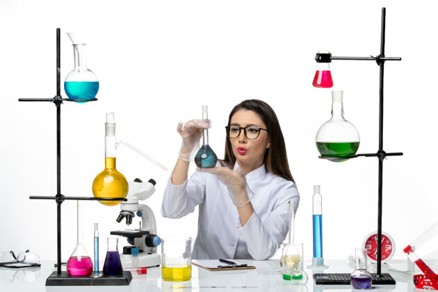 实验室前视图：身着白色医疗服的女化学家手持装有蓝色溶液的烧瓶 背景为白色实验室科学病毒冠状病毒大流行药品溶液科学