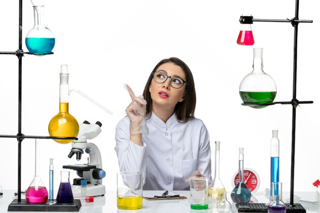 套装前视图穿着白色医疗服的女化学家正坐在白色背景上拿着解决方案科学大流行实验室病毒covid病毒烧杯实验