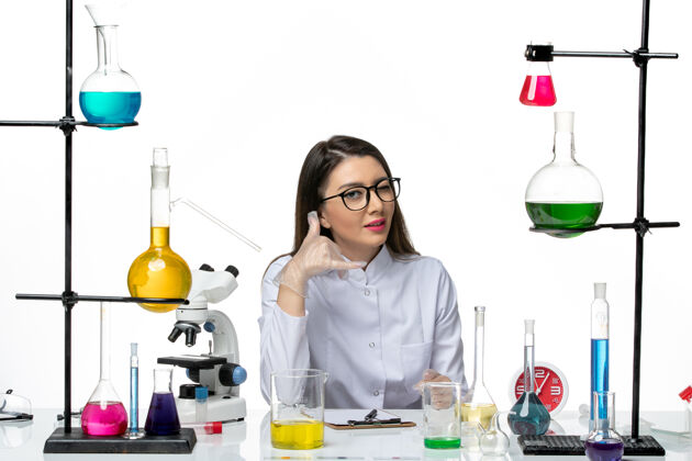 视图前视图穿着白色医疗服的女化学家正坐在一个白色背景的科学大流行实验室的病毒冠状病毒上前面病毒烧杯