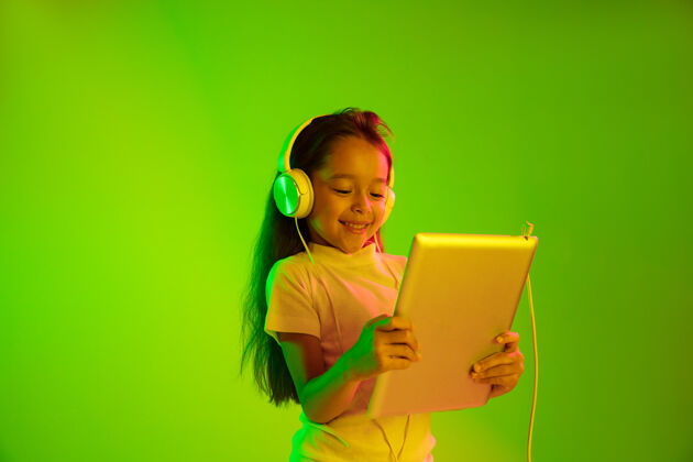孩子美丽的女性半身像 隔离在霓虹灯下的绿色背景上年轻感性的女孩人类情感 面部表情概念时尚的颜色使用平板电脑进行游戏 虚拟博客 自拍合成青少年惊讶