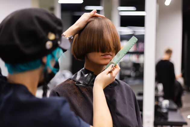 理发师一个专业的女理发师给客户理发这个女孩戴着面具坐在美容院里脸发型师面部