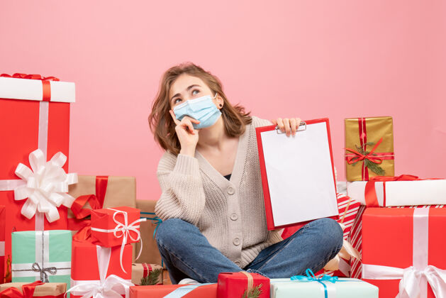 礼物正面图：坐在圣诞节周围的年轻女性戴着无菌面具出现礼物周围人