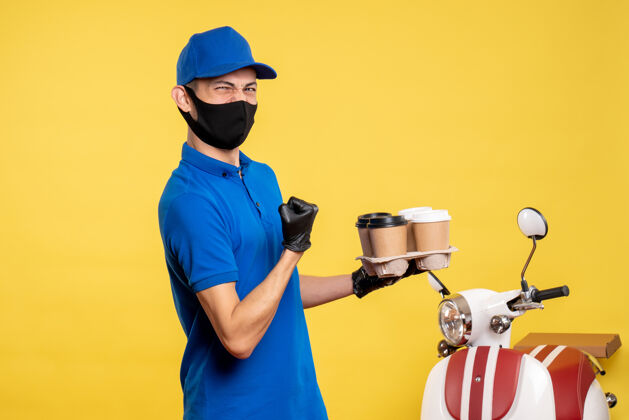 制服正面图：身穿蓝色制服 戴着面罩 手持咖啡的男性快递员 黄色工作服 covid-工作递送大流行咖啡男性信使蓝色