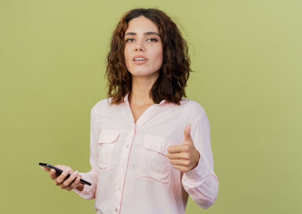 电话自信的年轻白种女人拿着手机 竖起大拇指 在绿色背景上 留着复印空间拇指女人年轻