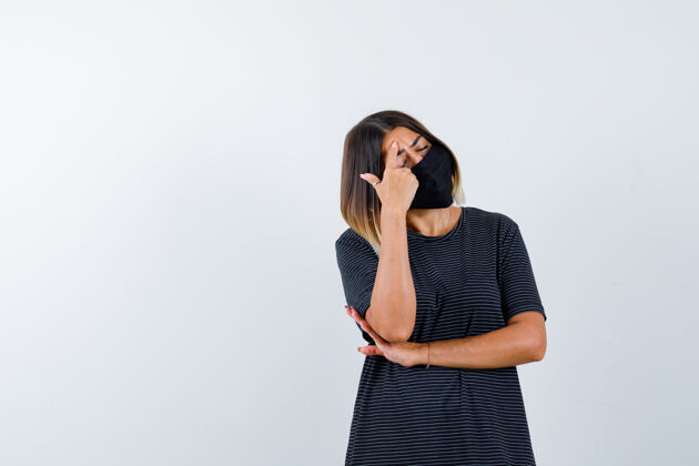 时尚一个穿着黑色衣服 戴着黑色口罩的年轻女子 把食指放在额头上 一只手放在胳膊肘下 看上去很疲惫 前视图护理皮肤黑发