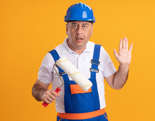 成年人焦急的白人成年建筑工人穿着制服站在那里 举起手 拿着橙色的滚轴刷手人制服