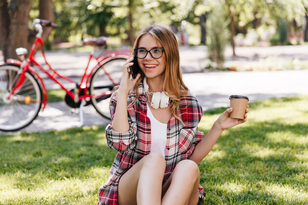 活动在公园喝咖啡的时候 一个幽默的高加索女孩给朋友打电话一张充满灵感的女士在草地上休息的户外照片金发女人大笑