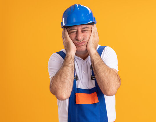 恼火恼怒的白人成年建筑工人穿制服把手放在脸上的橙色人手成年人