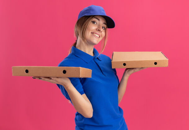 姿势穿着制服的年轻漂亮的送货女孩高兴地用两只手拿着比萨饼盒请手漂亮