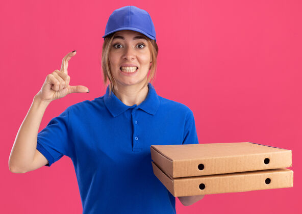 盒子一个穿着制服 拿着披萨盒的年轻漂亮送货女孩假装拿着粉红色的东西披萨制服东西