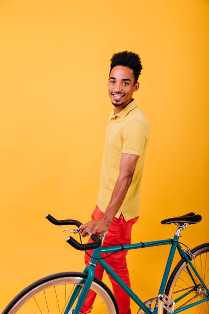 卷发兴奋的非洲男人穿着时髦的衣服和绿色的自行车合影室内照片中 微笑的黑人正在享受自行车男人时髦明亮