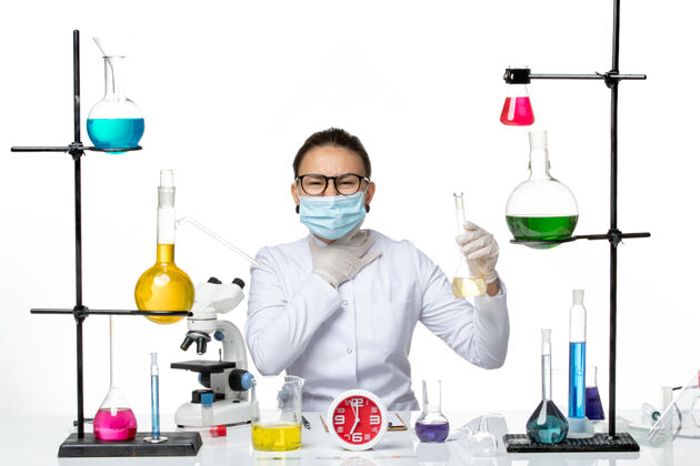 溶液前视图：穿着白色医疗服的女化学家 在浅白色背景上戴着面罩 化学家实验室病毒covid-splash医学实验室持有