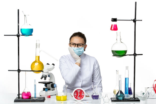 解决方案前视图穿着医疗服的女化学家带着面罩坐在浅白背景上的溶液化学病毒实验室病毒-飞溅化学飞溅病毒