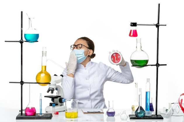 医生前视图穿着医疗服的女化学家戴着面具拿着时钟在白色背景上打哈欠病毒实验室化学冠状病毒-飞溅实验室西装飞溅