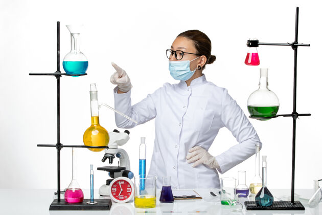 视图前视图身穿医疗服的女化学家戴着口罩 指着白色背景的病毒化学实验室covid-飞溅穿医院实验室