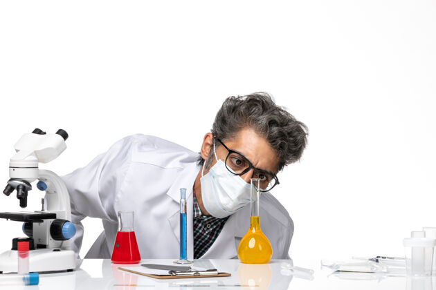 人正面近距离观察身着特殊套装的中年科学家 他们拿着溶液坐在白色背景上检查他们男性病毒科学冠状病毒-化学套装化学桌子