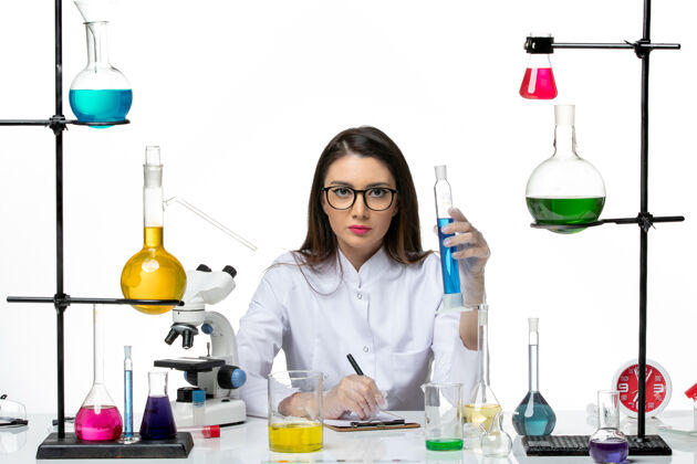 烧杯前视图穿着白色医疗服的女化学家拿着装有溶液的烧瓶在白色背景的科学病毒冠状病毒-大流行实验室研究正面实验