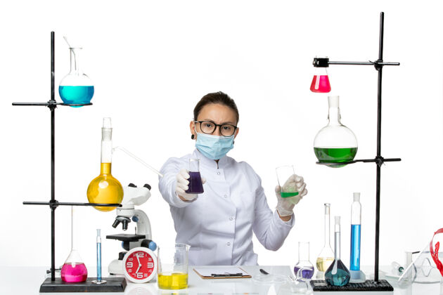 实验室前视图穿着医疗服的女化学家 戴着面罩 在白色背景上拿着不同的溶液 飞溅着病毒化学实验室的病毒视图化学医学