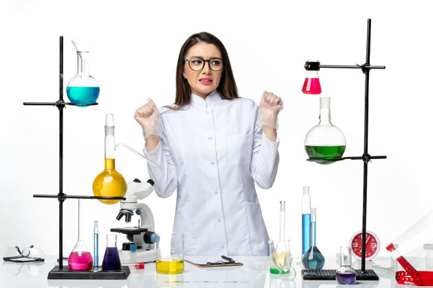 立场正面图：穿着无菌医疗服的女化学家站在桌子旁 拿着白色背景病毒疾病病毒的解决方案-大流行科学医生解决方案外套