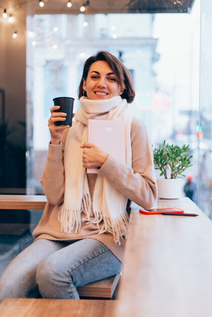 冬天一个女孩在舒适的咖啡馆里用一杯热咖啡取暖日记微笑成人