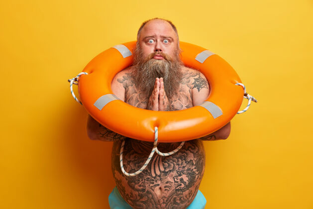 允许乞讨者双手合十 请求许可 身上有纹身 大肚子 摆着充气救生圈 隔离在黄色墙壁上超重的家伙要去游泳超重安全胡子