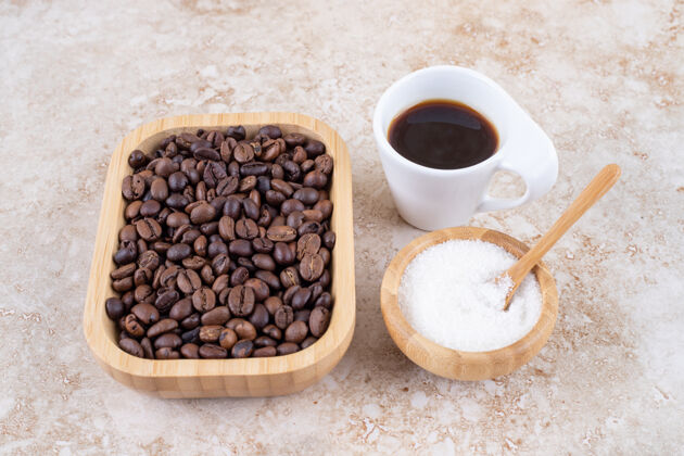 糖一堆咖啡豆放在木盘里 旁边是一小碗糖和一杯咖啡勺子美味