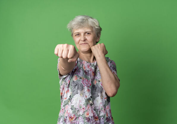 老高兴的老妇人把拳头放在绿色的墙壁上 随时准备出击拳准备绿