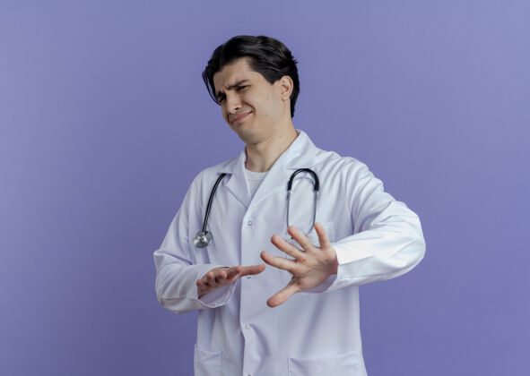 长袍穿着医用长袍和听诊器的年轻男医生看起来没有做任何孤立的动作穿着手势听诊器