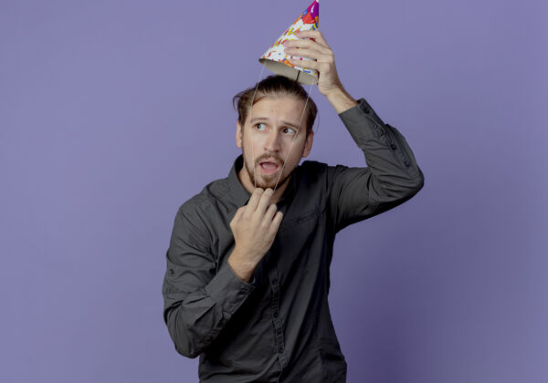 男人焦急的帅哥戴着生日帽 望着紫色墙上孤零零的一面帽子紫色抱着