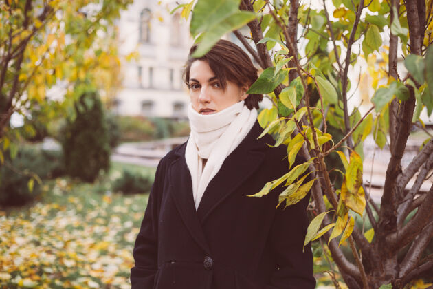 优雅公园里穿着冬天黑外套白围巾的女人的户外肖像温暖树叶时尚