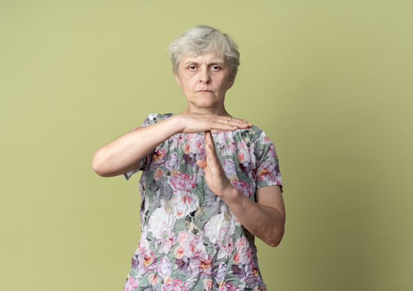 绿色自信的老妇人在橄榄绿的墙上做手势暂停手势时间橄榄手势
