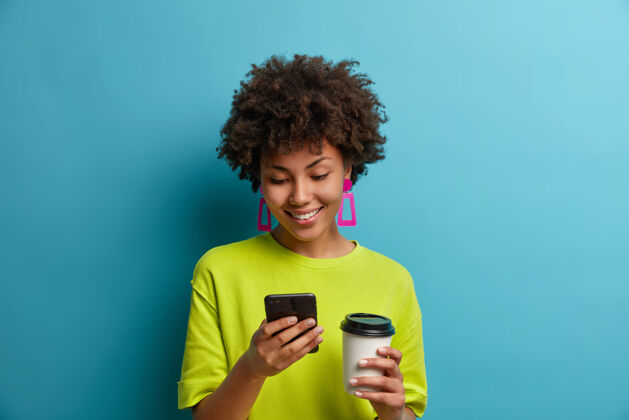 高兴快乐积极向上的民族女青年在手机上输入信息或拨打电话号码 喝外卖咖啡 使用在线移动应用程序 搜索网页 阅读博客和社交网络聊天检查喜悦搜索