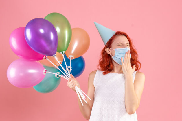 病毒正面图年轻女性手持彩色气球在粉红色的面具上年轻女性乐趣快乐