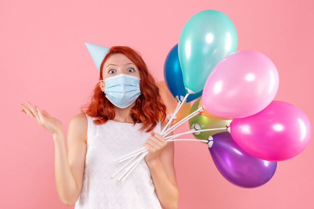 正面正面图年轻女性手持彩色气球在粉红色的面具上病毒视图生日