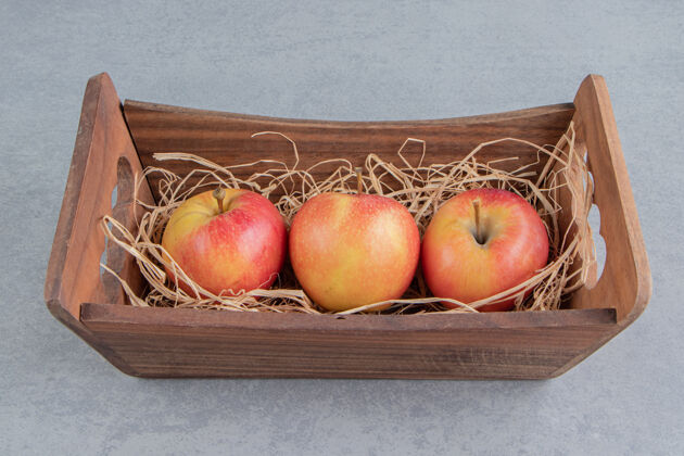 多汁苹果和稻草堆在大理石上的木篮里健康美味篮子
