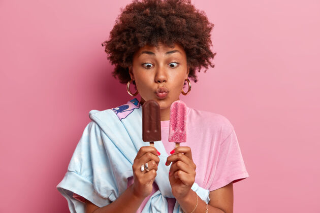 黑发有趣少女的照片保持嘴唇圆润 看着开胃的冰淇淋 享受夏天的时光 喜欢冷甜点 穿着时髦的服装 选择巧克力和草莓口味香草青少年光滑