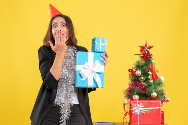 圣诞节圣诞节心情与情感美丽的女士与xsmas帽子举行的礼物 并在黄色的办公室沉默的姿态帽子人成人