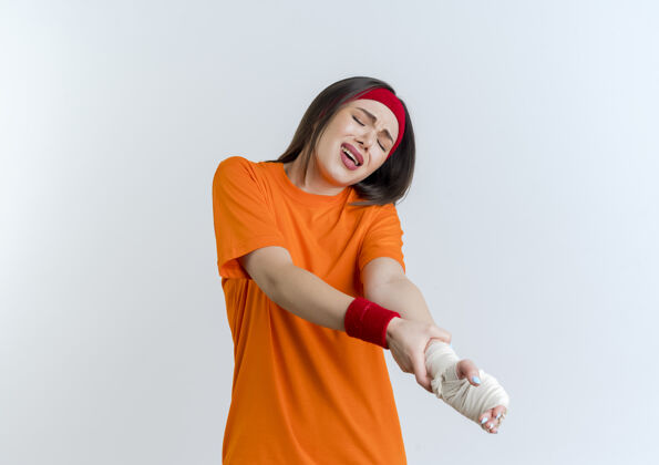 包裹疼痛的年轻运动女性戴着头带和腕带抱着受伤的手腕缠着绷带闭着眼睛女人年轻运动