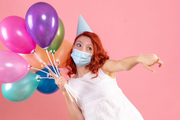 流行正面图年轻的女性手持彩色气球在面具上浅粉色人圣诞节病毒