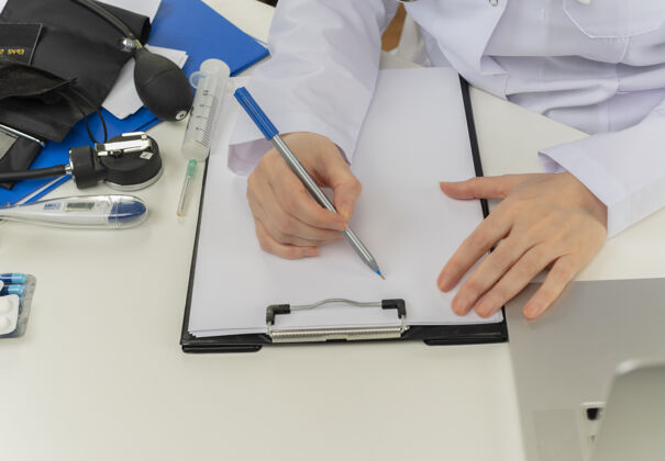工作一张女医生手拿着医疗工具和笔记本电脑在写字台上写处方的剪贴照片成人医生女性