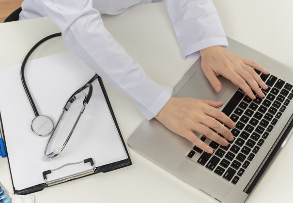 医生一张女医生手拿着笔记本电脑在办公桌上用医疗工具和剪贴板工作的剪贴照片工具剪贴板成人