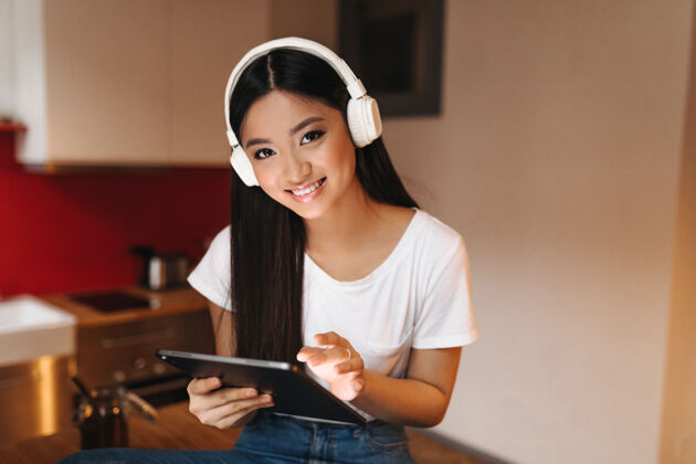 魅力一位黑发少女面带微笑 望着前方 手持平板电脑 戴着耳机听音乐互联网歌曲女性