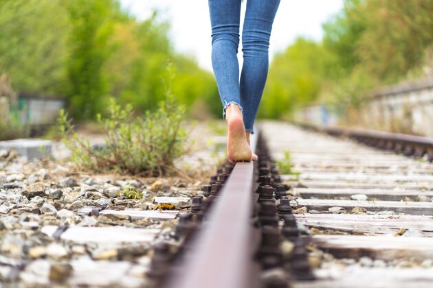 女人穿着牛仔裤的女人赤脚穿过火车铁轨步行道路运输