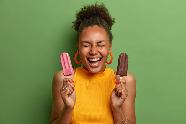 青少年不健康的食物和减肥概念积极微笑的女人闭着眼睛笑 拿着草莓冰棒和巧克力冰淇淋 隔离在绿色的墙上夏天 吃味道年轻女人