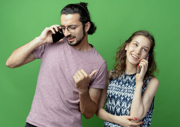 电话一对年轻的男女 站在绿色的背景下 愉快而积极地用手机交谈年轻手机情侣