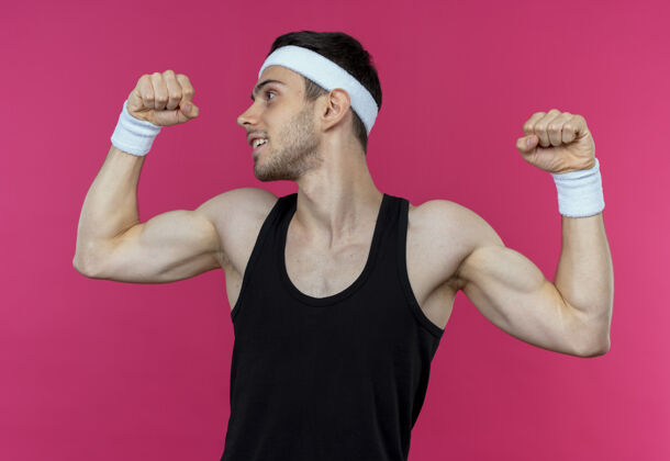 举起戴着头巾的年轻运动型男子举起拳头展示肱二头肌 站在粉色背景上的赢家概念运动年轻拳头