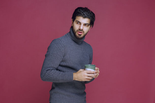 年轻一个穿着灰色毛衣的男人手里拿着一个咖啡杯年轻人服装员工